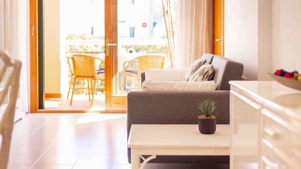 Ein modernes Wohnzimmer mit einem grauen Sofa, einem kleinen weißen Tisch und einer Topfpflanze.