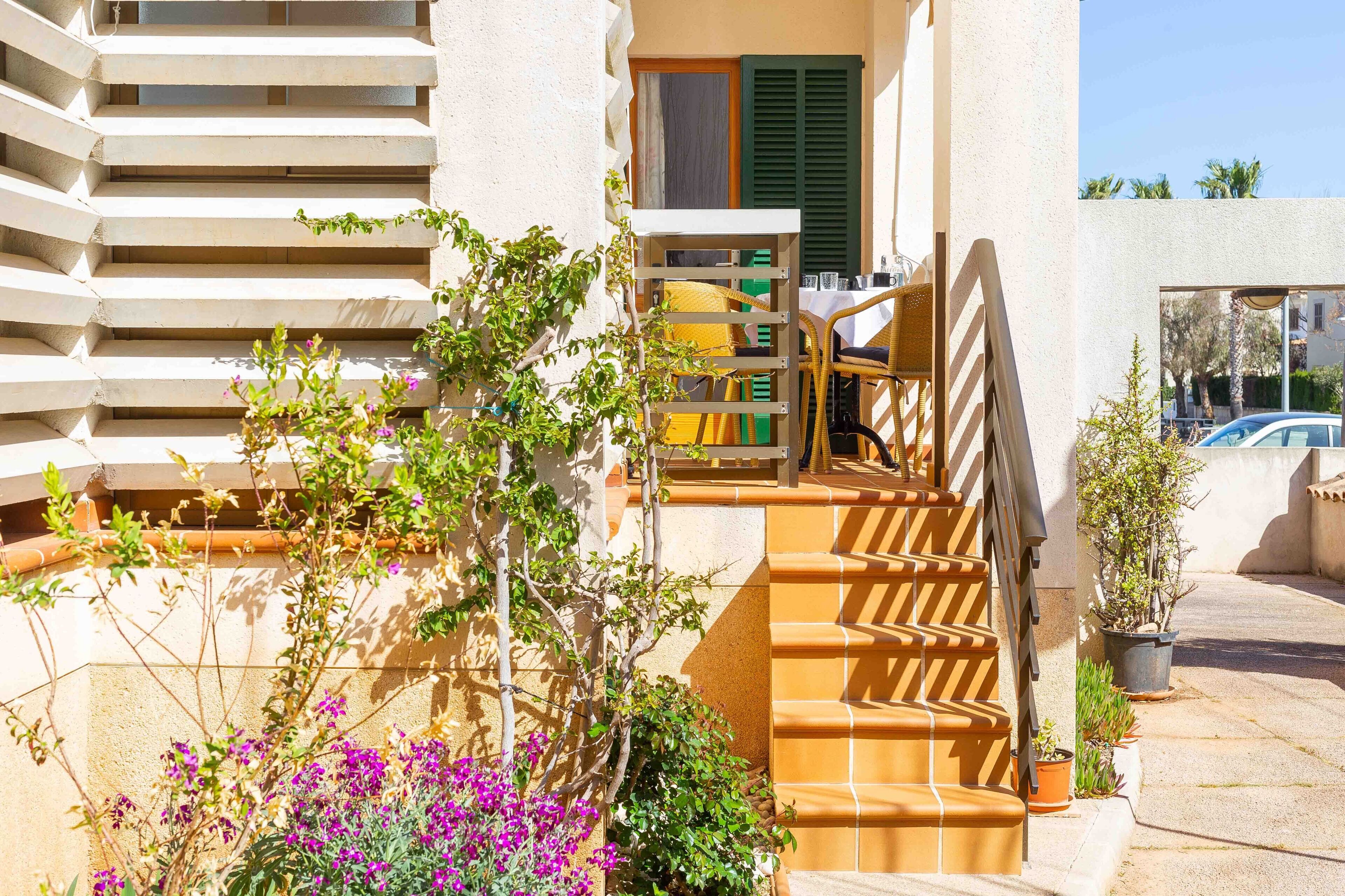 Un immeuble d’habitation avec un escalier menant à un balcon, lequel est entouré de plantes et de fleurs en pot.