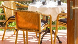 Eine Terrasse im Freien mit Korbstühlen und einem Esstisch, mit Blick auf ein Wohngebäude.
