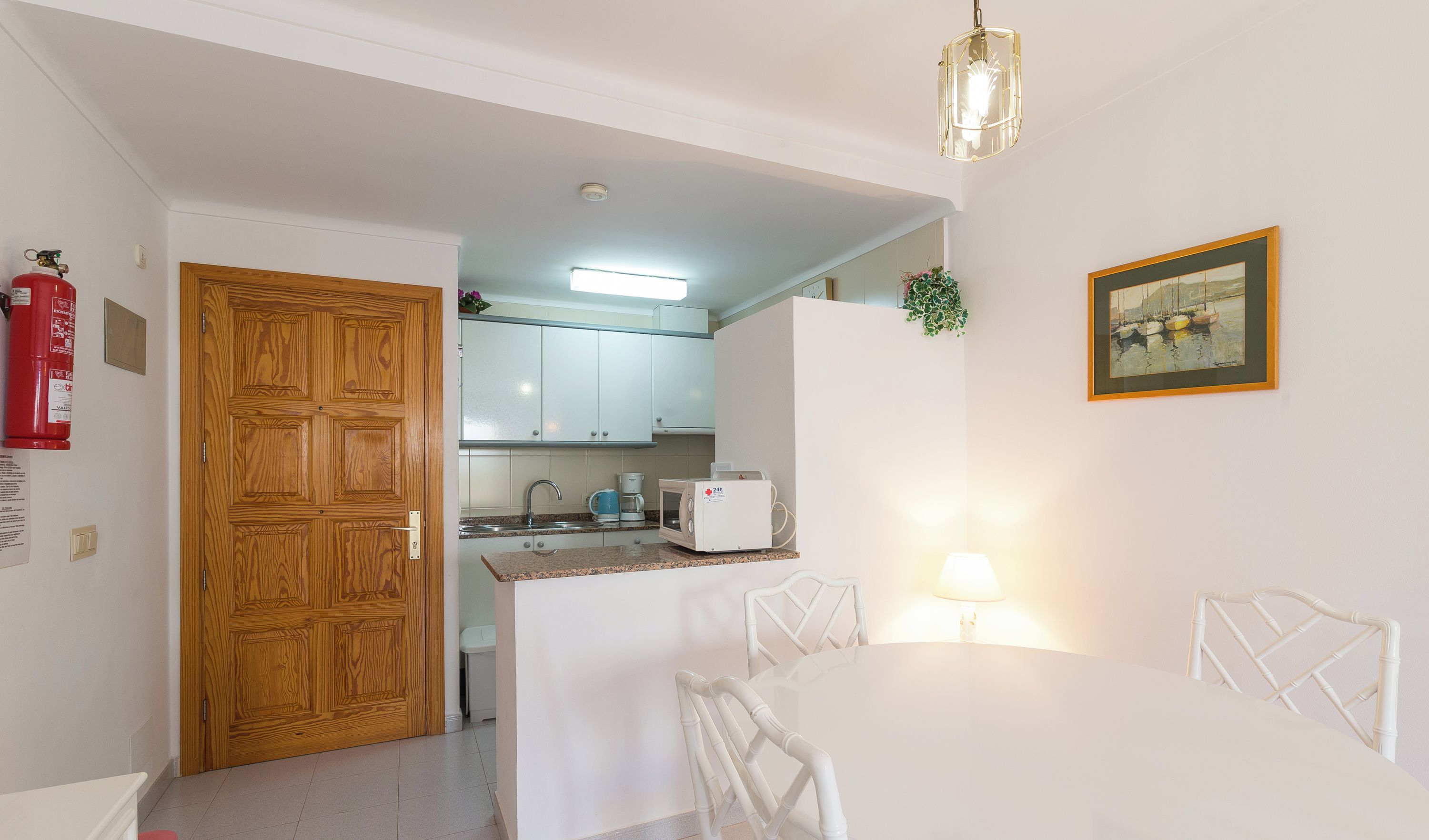 Une cuisine compacte avec des meubles blancs, une porte en bois et un coin repas comprenant une table et des chaises blanches.