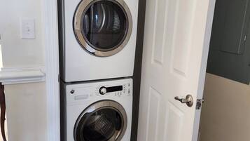 Un lavadero compacto con dos lavadoras apiladas y un estante pequeño encima.