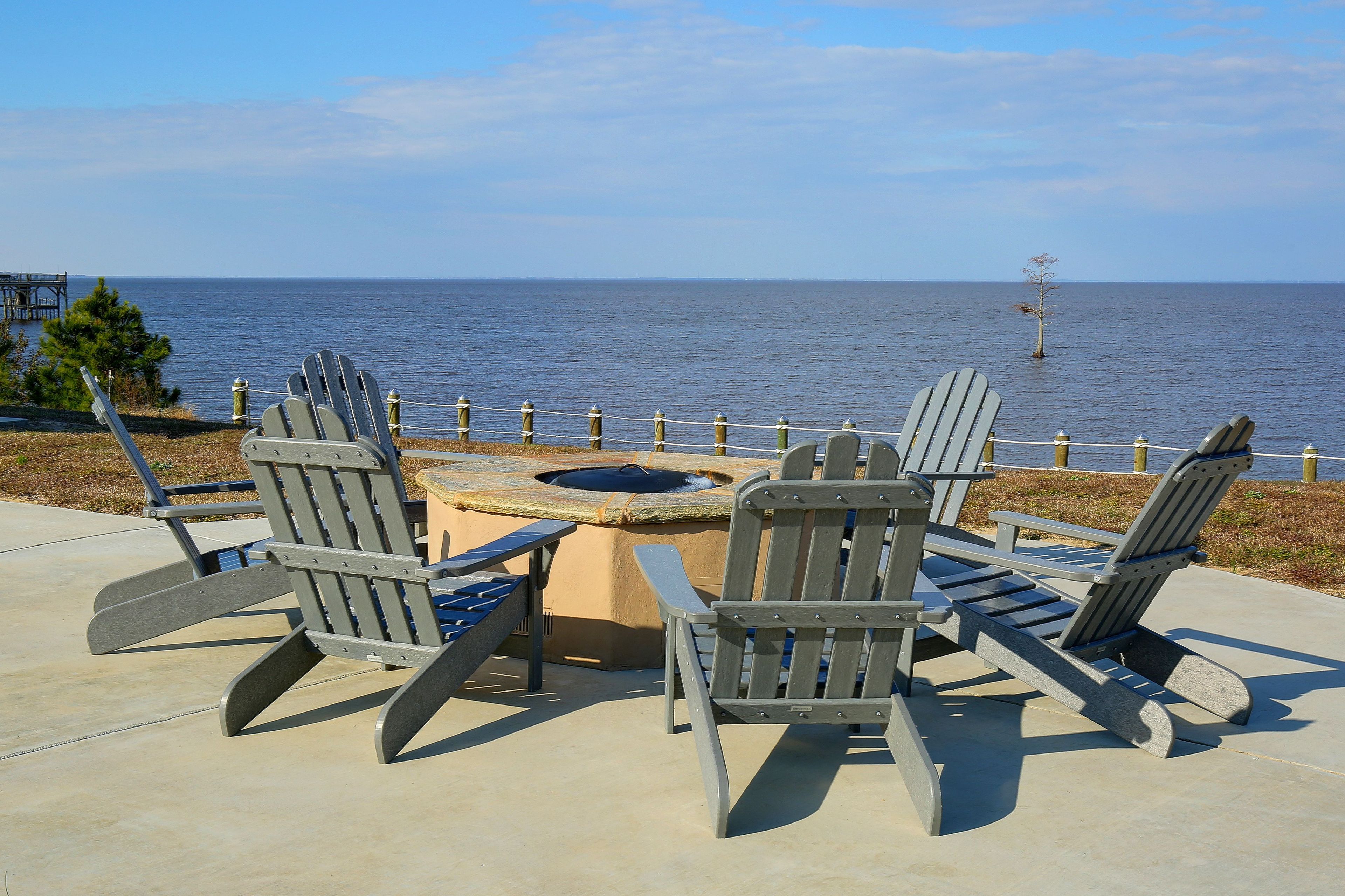A deck with Adirondack chairs and a fire pit overlooking the ocean.