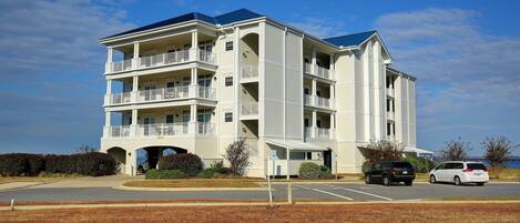 A multi-story hotel with a central entrance, balconies, and a parking lot.