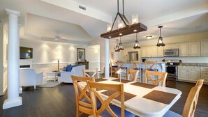A modern kitchen with white cabinets, a dining area with a large table and chairs, and a living room with a sofa and coffee table.