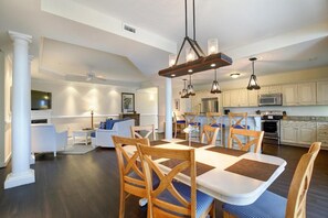 A modern kitchen with white cabinets, a dining area with a large table and chairs, and a living room with a sofa and coffee table.
