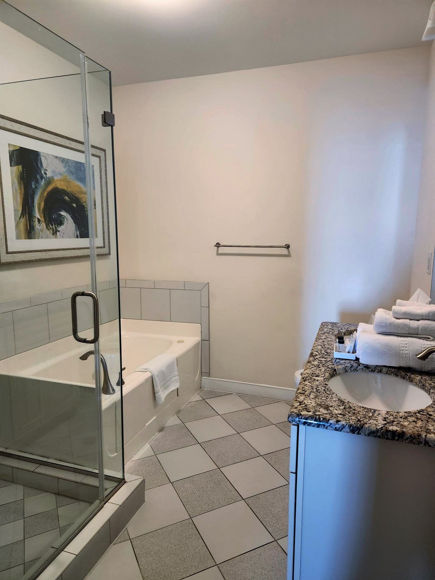 A bathroom with a glass-enclosed shower, a bathtub, and a granite countertop sink.