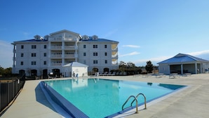 A swimming pool with a clear blue water, surrounded by a concrete deck, and a large building with multiple balconies in the background.