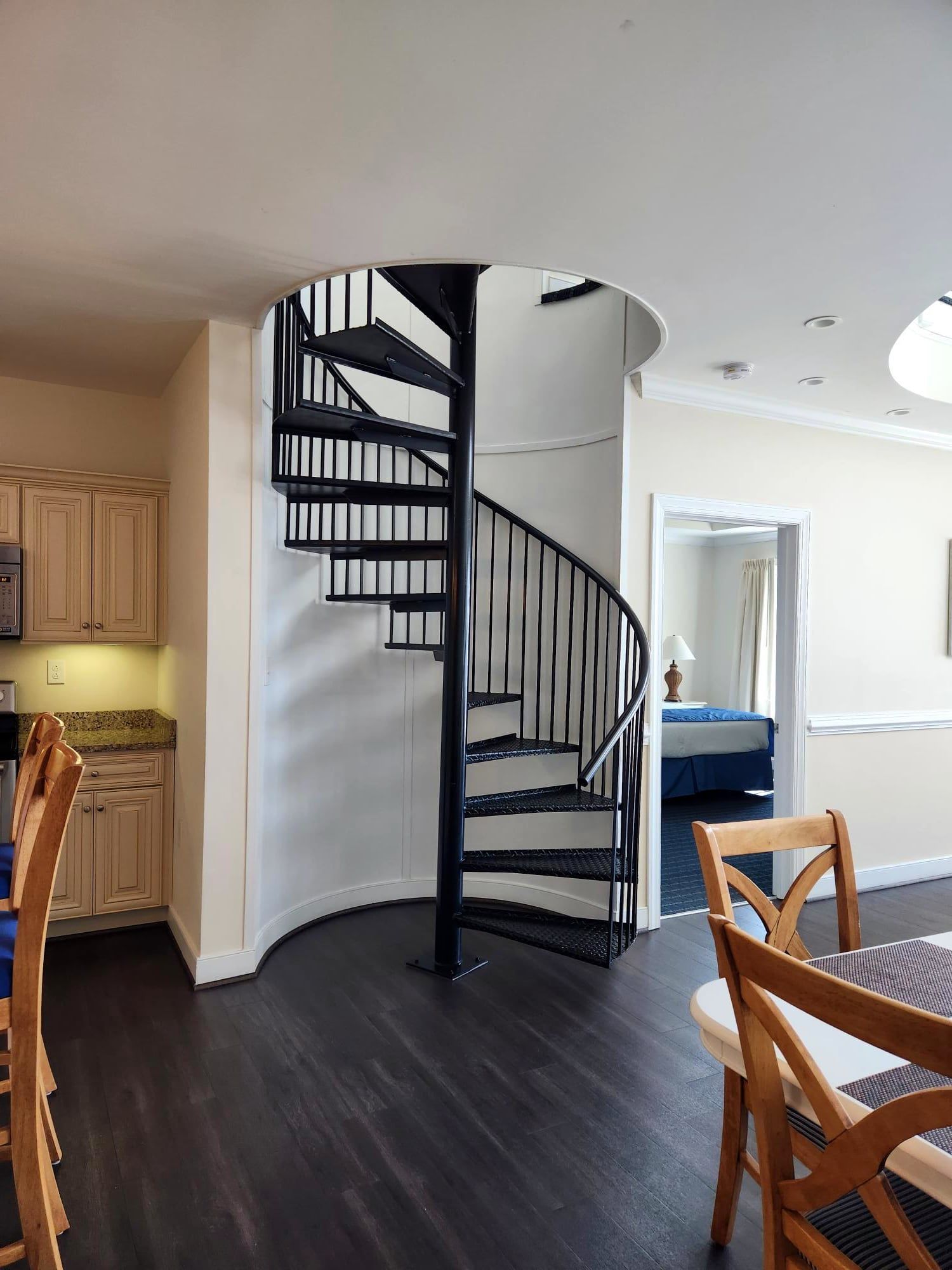 A modern interior with a spiral staircase, wooden dining table, and kitchen cabinets.