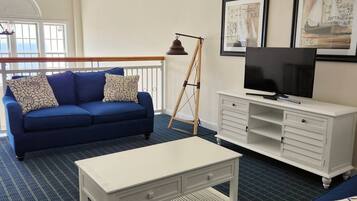 A modern living room with a blue sofa, white coffee table, and a TV on a white cabinet.