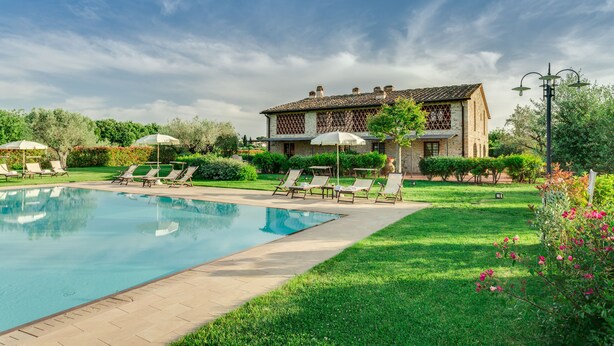 A swimming pool with lounge chairs and umbrellas, surrounded by a well-maintained lawn and a building with a tiled roof. - Il Pollaio, one bedroom apartment walking distance to Tavarnelle Val di Pesa (Tavarnelle Val di Pesa)