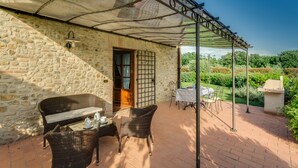 A stone building with a covered patio area featuring wicker furniture and a table set for two. - Il Pollaio, one bedroom apartment walking distance to Tavarnelle Val di Pesa (Tavarnelle Val di Pesa)