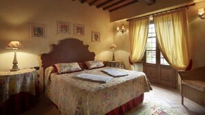 A bedroom with a wooden ceiling, floral bedspread, and a window with curtains. - Il Pollaio, one bedroom apartment walking distance to Tavarnelle Val di Pesa (Tavarnelle Val di Pesa)