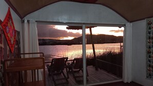 Une pièce dotée d’une grande porte-fenêtre coulissante qui donne sur une terrasse offrant une vue sur un plan d’eau au coucher du soleil.