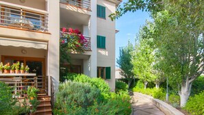 A multi-story building with balconies, a garden with various plants and flowers, and a paved pathway.
