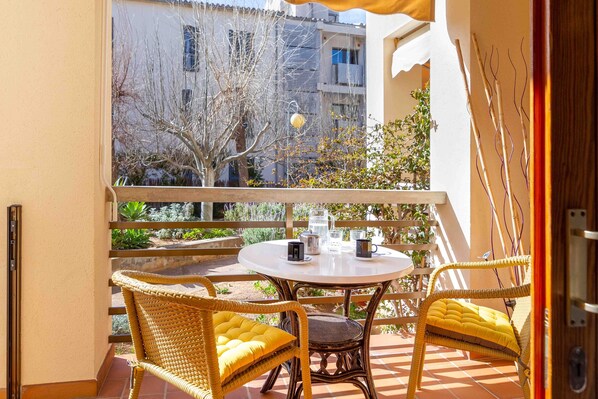 A balcony with wicker chairs and a table, a view of buildings and trees, and a door with a wooden frame.