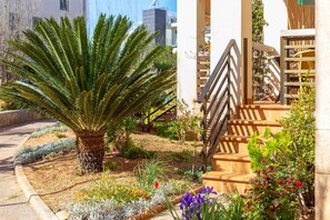 A well-maintained garden with a palm tree, various plants, and a wooden staircase leading to a building.