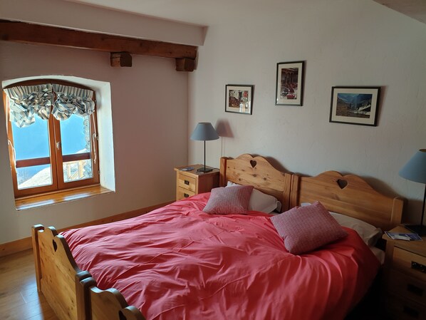 Ein Schlafzimmer mit einem hölzernen Bett, einem Fenster mit Vorhängen, einem Nachttisch mit Lampe und drei gerahmten Bildern an der Wand.