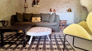 Una sala de estar acogedora con pared de piedra, un sofá gris, un tapete estampado, una mesita redonda y un sillón amarillo.