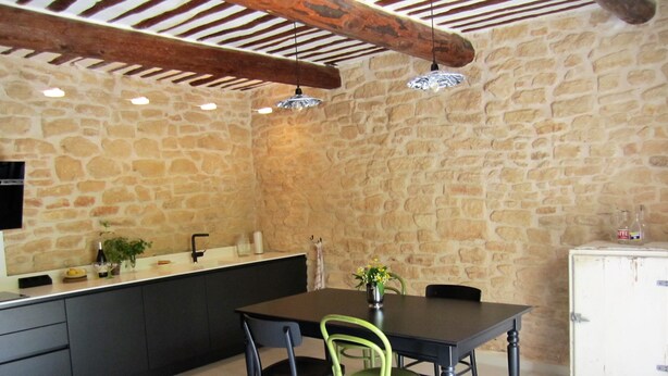 Cocina con paredes de piedra, una mesa de comedor y sillas, un armario blanco y una lámpara colgante.