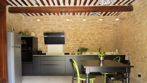 Una cocina con pared de piedra, horno empotrado, refrigerador y comedor con mesa y sillas.