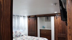 Ein Schlafzimmer mit Bett, Holzschrank und einem kleinen Bad mit Spiegel und Waschbecken.