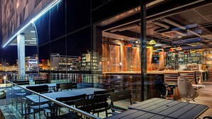 An outdoor dining area with tables and chairs, a glass railing, and a view of the cityscape at night. - Radisson blue riverside (Göteborg)