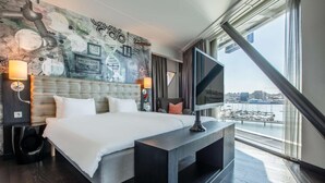 A modern hotel room with a large bed, a television, a view of the water, and a mural on the wall. - Radisson blue riverside (Göteborg)