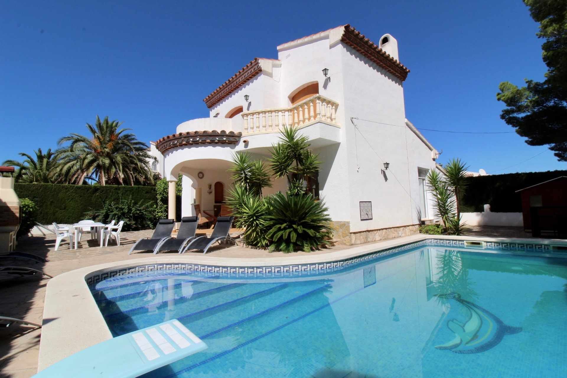 A white villa with a swimming pool, outdoor seating, and palm trees.