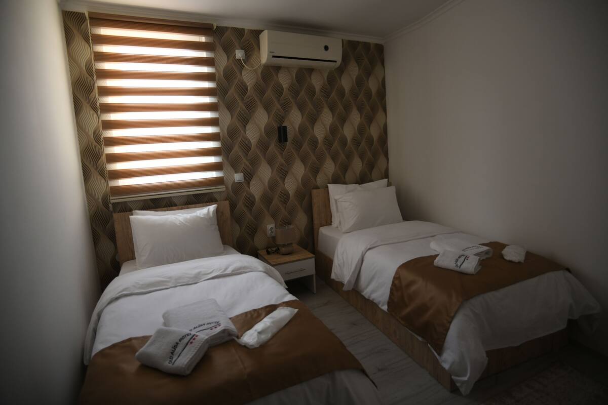 A hotel room with two beds, a patterned wall, and an air conditioning unit.