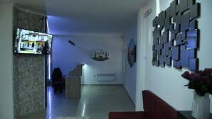 A living room with a TV, a red sofa, a chessboard, and a wall with framed pictures. - Hotel Old Alisa (Skopje)