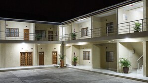 Un edificio de varios pisos con un patio central, con balcones, plantas en macetas y una escalera que conduce a un nivel superior.