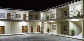 Un edificio de varios pisos con un patio central, con balcones, plantas en macetas y una escalera que conduce a un nivel superior.