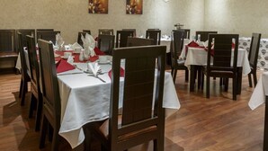 Un comedor con varias mesas y sillas, cada conjunto con manteles blancos y servilletas rojas.
