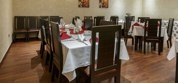 Un comedor con varias mesas y sillas, cada conjunto con manteles blancos y servilletas rojas.