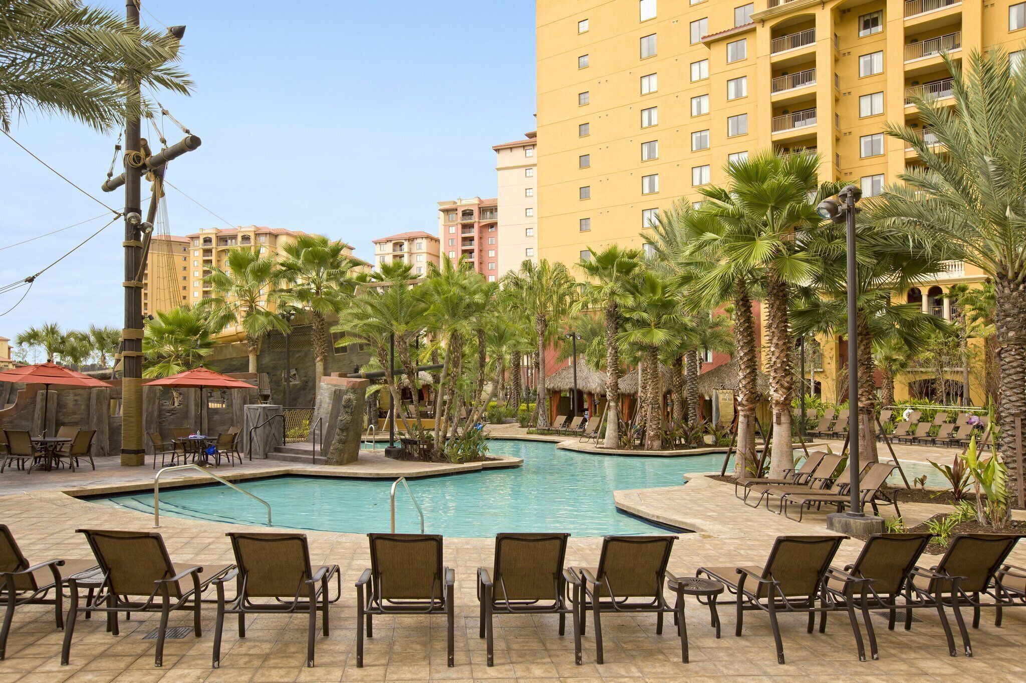 A pool area with lounge chairs and palm trees, surrounded by high-rise buildings.