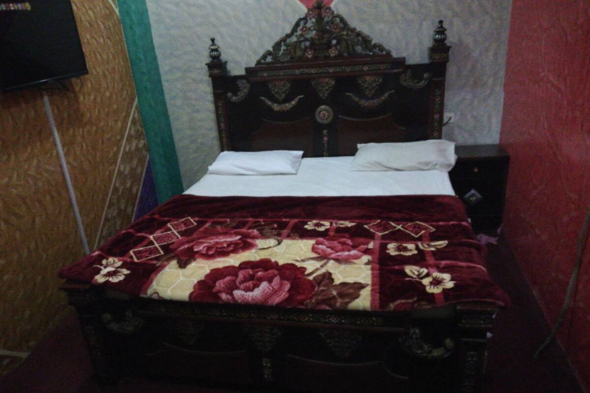 A bed with a floral bedspread, a wooden headboard, and a white pillow.