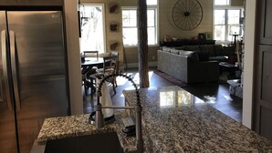 Eine geräumige Küche mit Granit-Arbeitsplatten, ein Essbereich mit Tisch und Stühlen sowie ein Wohnzimmer mit Sofa und einem großen Fenster.