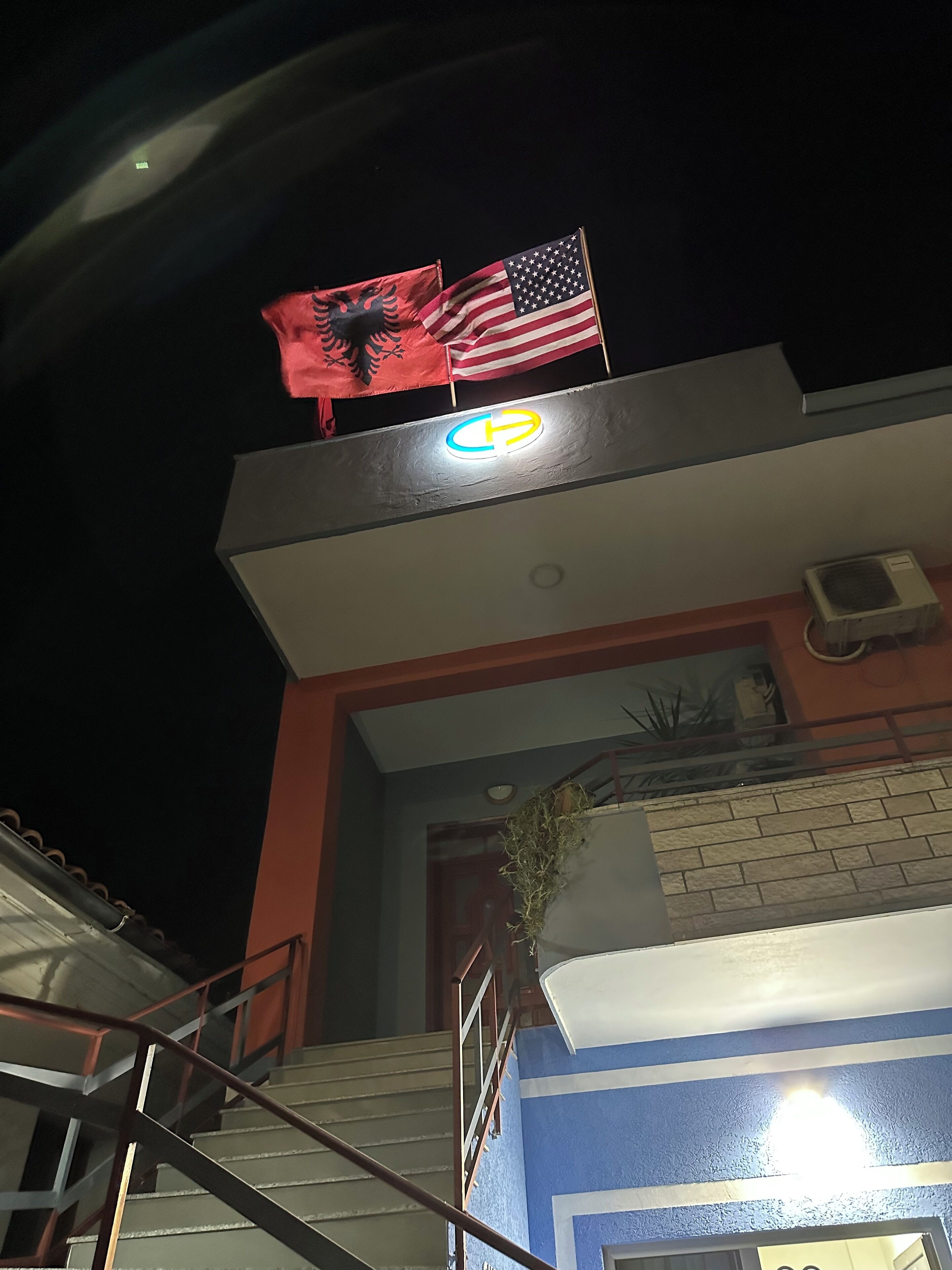 A building with a staircase, a flag, and a sign with a circular symbol.