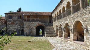 Une cour bordée de bâtiments en pierre, une arche centrale et un escalier menant aux étages supérieurs.