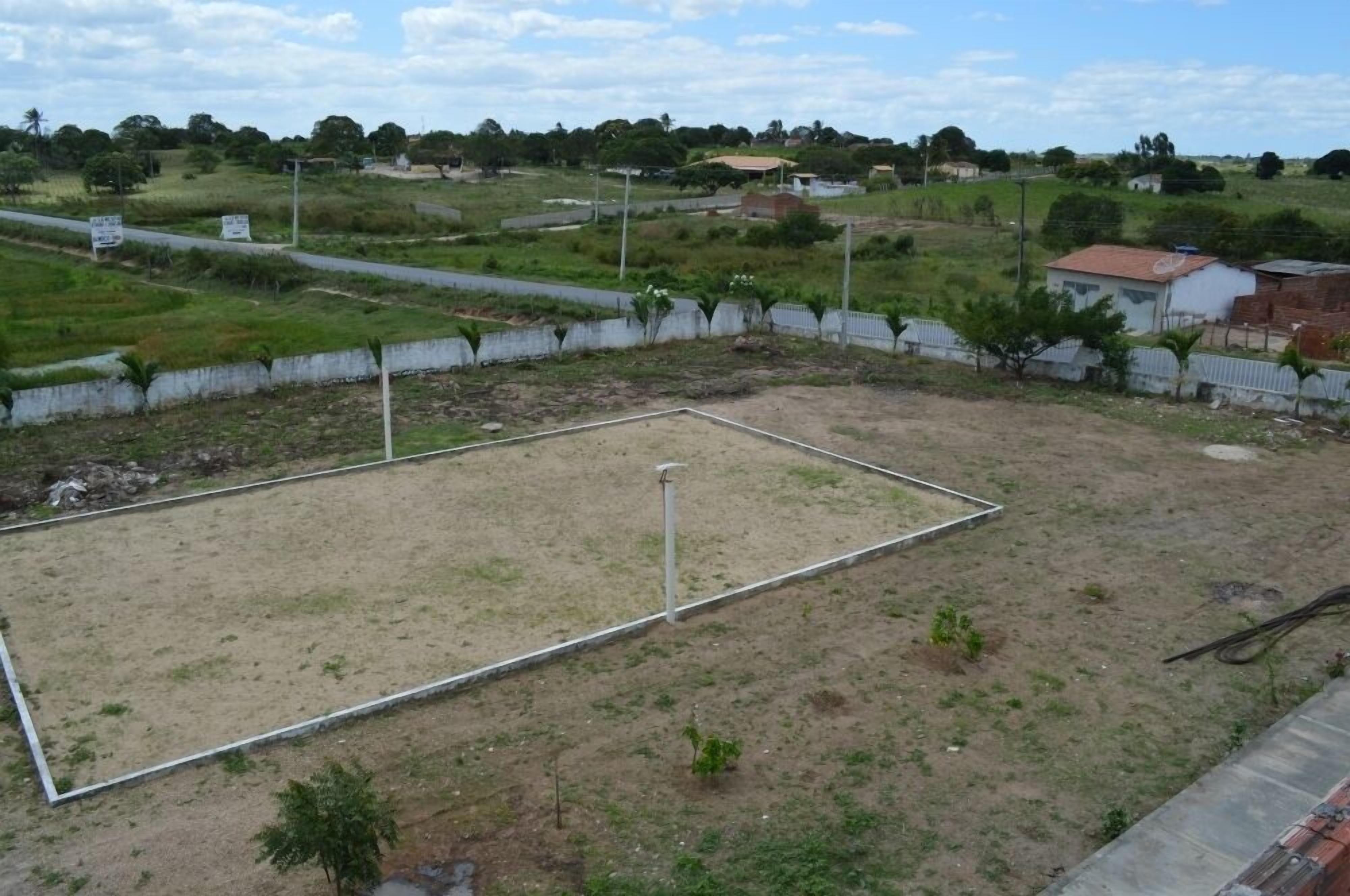 An outdoor area with a fenced sports court, surrounded by greenery and residential buildings.