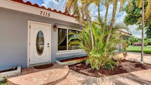 Ein Haus mit der Nummer 7115 an der Tür, einem Vorbau und einer Palme im Garten.