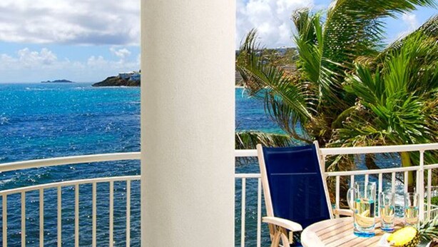 Ein Balkon mit Blick auf das Meer, ein Tisch mit Getränken und einer Ananas sowie ein blauer Stuhl.