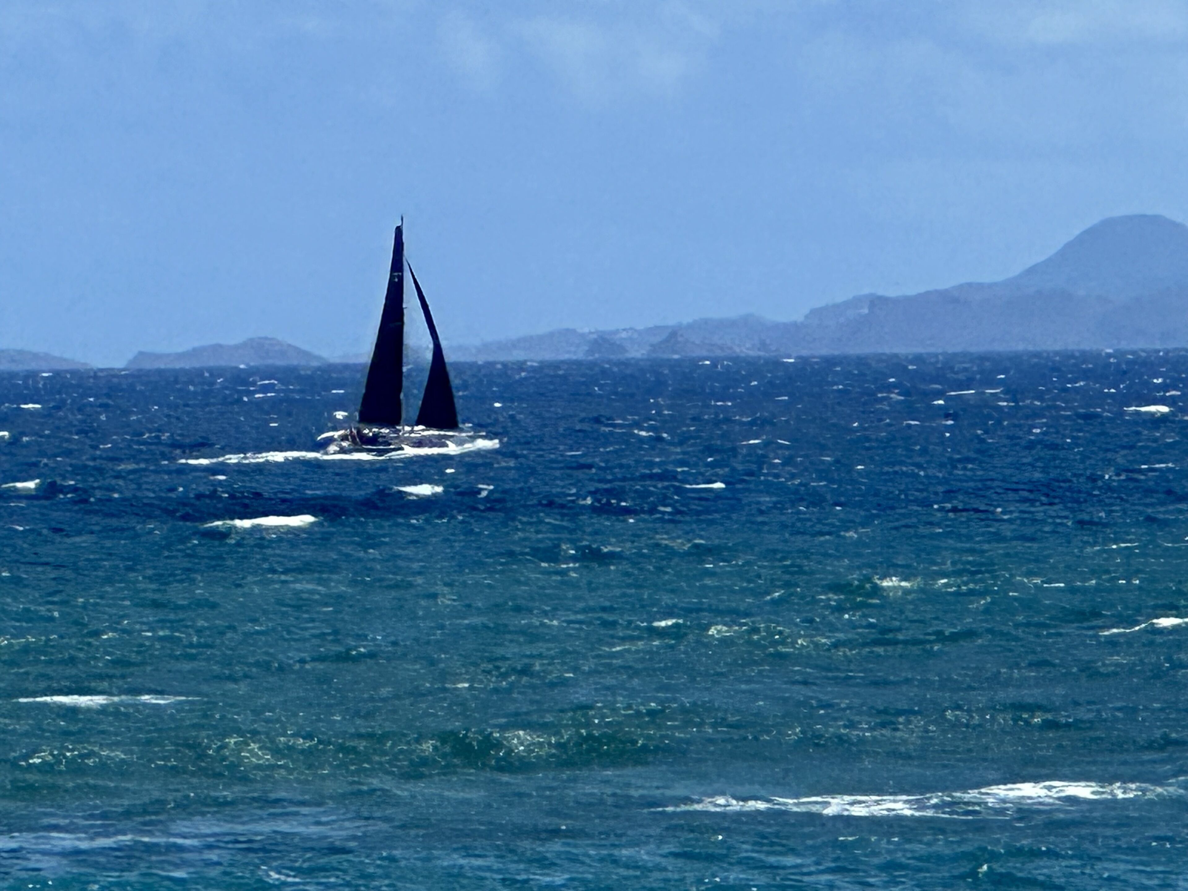 A sailboat on a vast ocean with distant mountains.