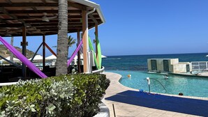 Ein überdachter Poolbereich mit Blick auf das Meer, einer Palme und Liegestühlen.