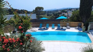 A swimming pool with lounge chairs and umbrellas, surrounded by stone tiles and plants. - Superior 3-room villa (FREJUS)