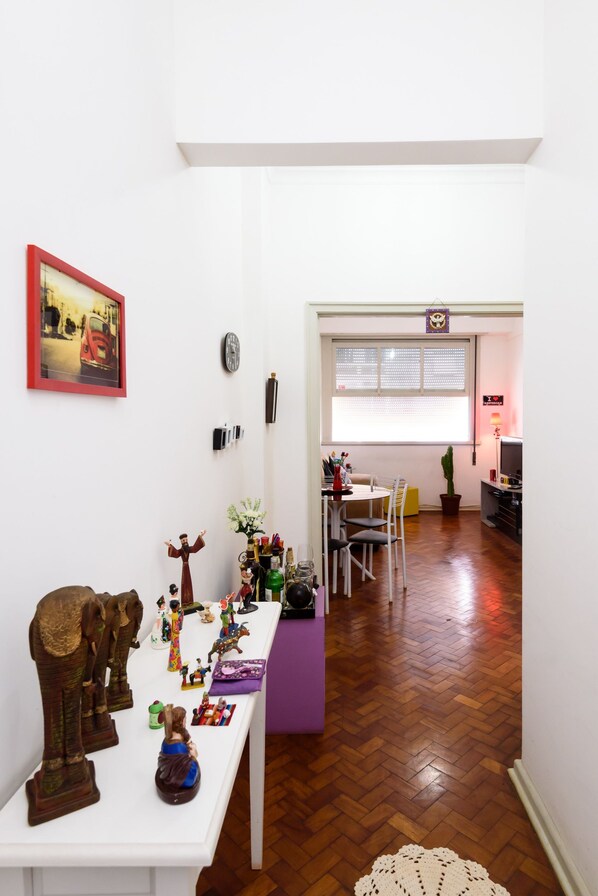 A hallway with a white table displaying various decorative items, a purple bench, and a wooden floor.