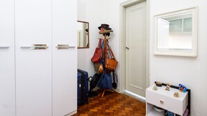 A hallway with a wooden floor, a coat rack with various bags, a suitcase, and a small cabinet with decorative items. - Omar do Rio - NSC1001 (Rio de Janeiro)