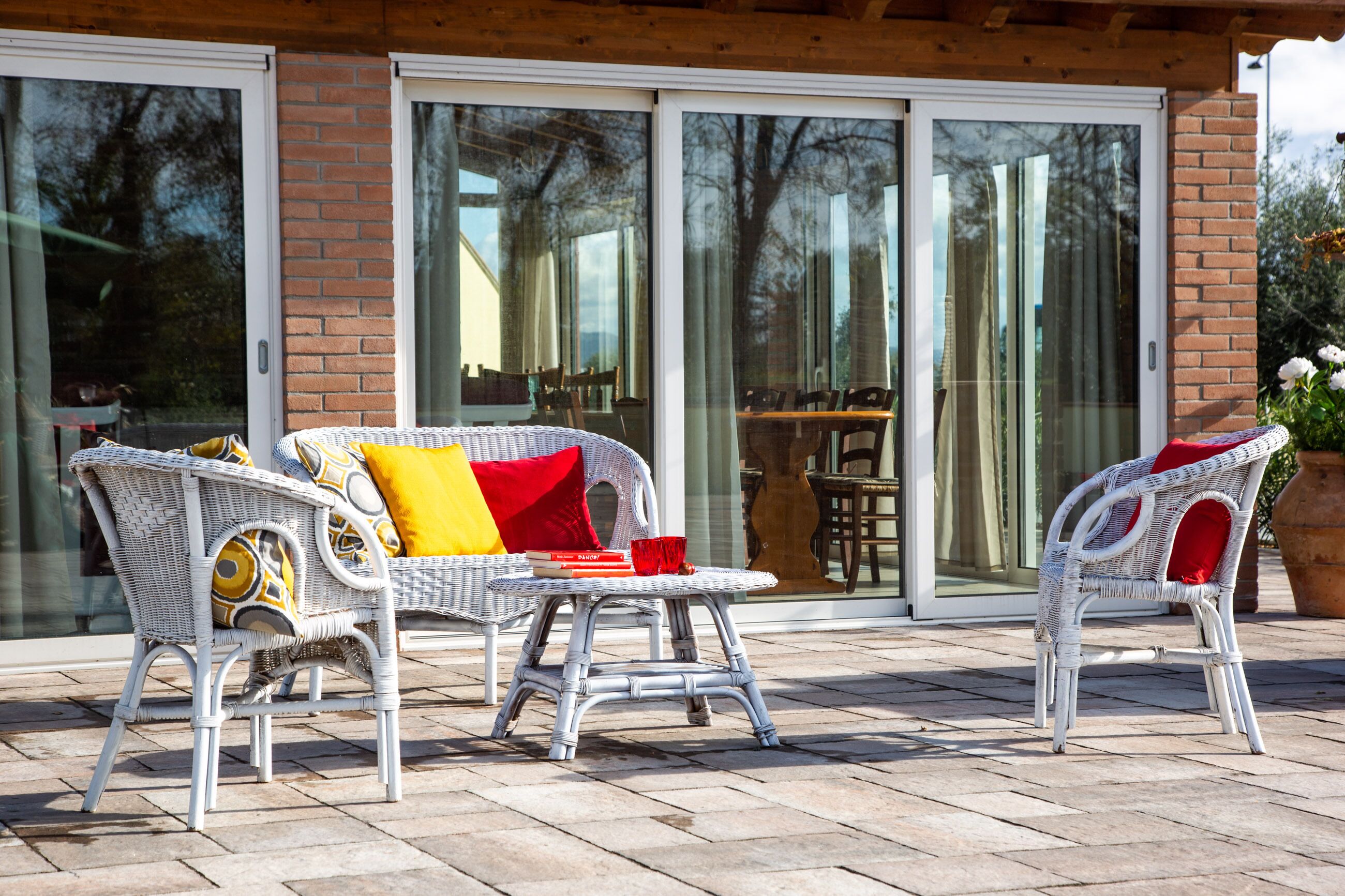 Un patio con mobiliario de mimbre y una puerta corrediza de vidrio que da a un espacio interior.