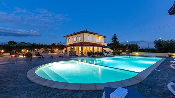 A swimming pool with lounge chairs and a building in the background. - Il Nocciolo 12, Emma Villas (Cecina)