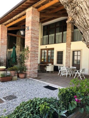 A covered outdoor patio with a brick column, a table with chairs, and potted plants.